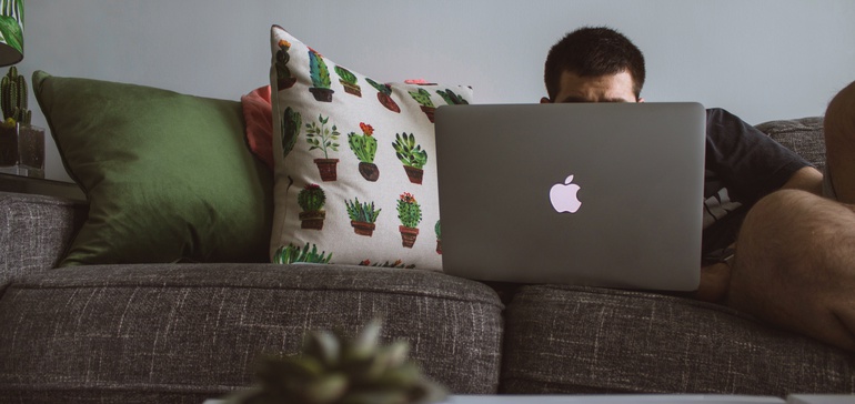 Student casually works on laptop from the comfort of his couch.