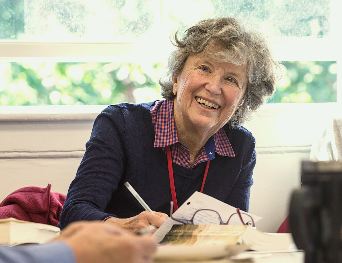 An older woman smiles while sitting in an HILR classroom. She is looking off camera at someone.