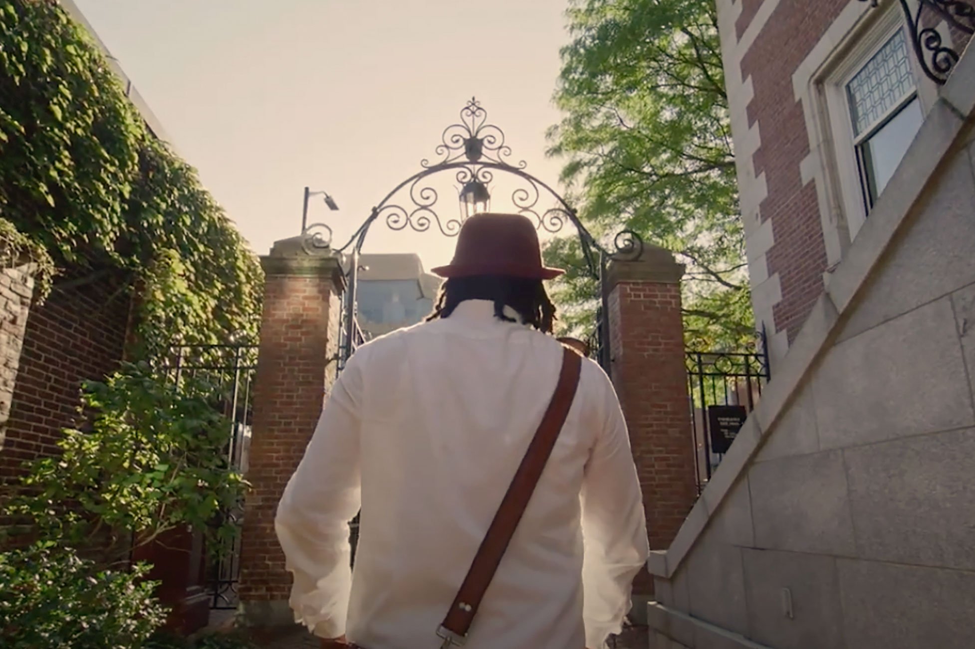 A photograph of a man walking through one of the Harvard gates, his back to the camera.